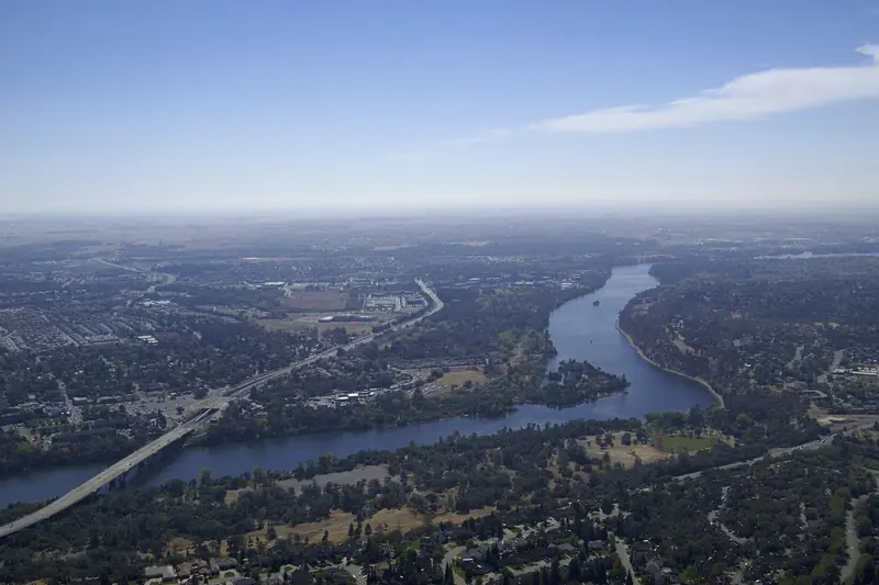 The American River curving through wooded suburbs near Fair Oaks, seen from the air on a hazy day